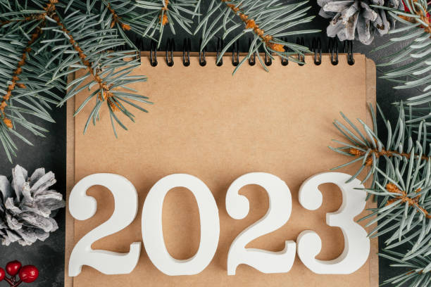 Happy New Year 2023. White numbers 2023 lying on folded notebook with Christmas tree branches and pine cones, copy space stock photo