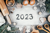 Numbers 2023 written on flour with branches of Christmas tree, baking accessories and ingredients. Happy New Year 2023