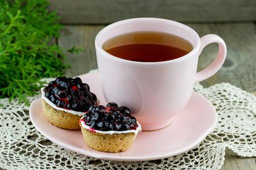 Currant cakes on pink plate with cup of tea on wooden background. Christmas (New Year) composition