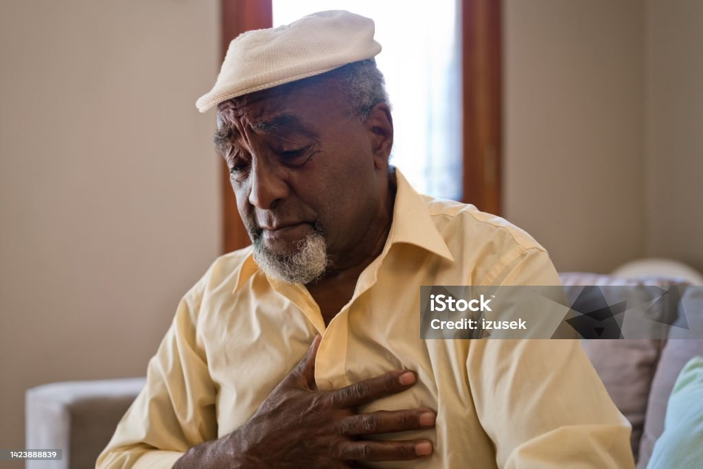 Elderly man having pain in chest at home Senior man suffering from pain in chest. Elderly male is having heart attack. He is sitting on sofa. Men Stock Photo