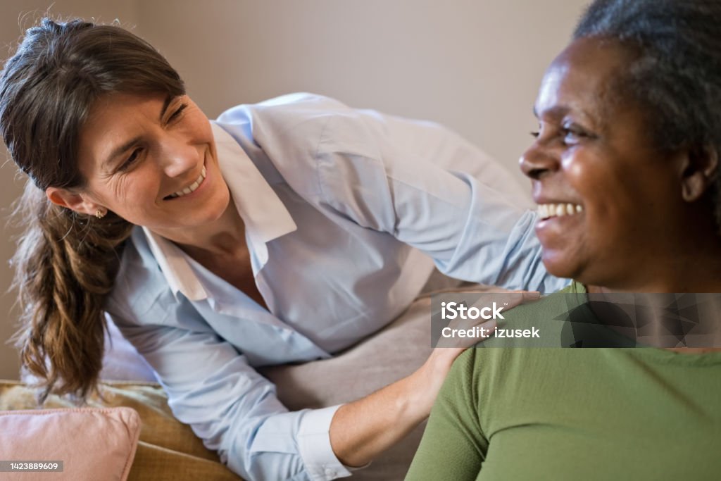 Female nurse with senior woman at home Smiling home caregiver talking with senior woman. Nurse is with elderly female at home. They are looking at each other. Honesty Stock Photo