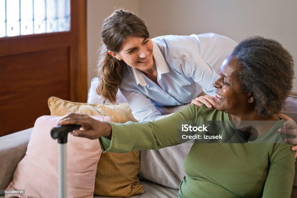 Female nurse with senior woman at home Smiling home caregiver talking with senior woman. Nurse is with elderly female at home. They are looking at each other. 70-79 Years Stock Photo