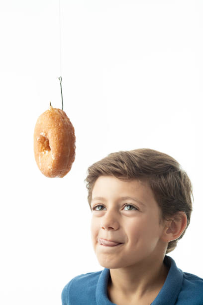 un enfant regarde avec nostalgie un beignet suspendu à un crochet. - longingly photos et images de collection