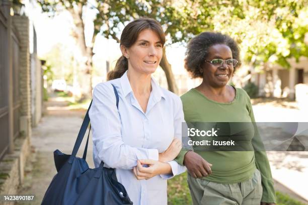 Nurse And Senior Woman Walking On Footpath Stock Photo - Download Image Now - Nurse, Purse, Active Lifestyle