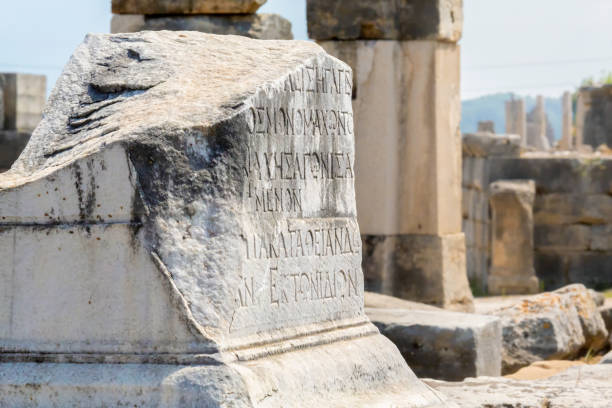 antigua inscripción griega tallada en la piedra. ruinas desenfocadas al fondo. perge, o perga es la antigua ciudad de anatolia en pamphylia. región de antalya, turquía (turkiye). enfoque seleccionado, espacio de copia - roman antalya turkey restoring fotografías e imágenes de stock