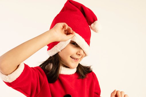 Little girl in santa costume playing with santa head in front of white background.