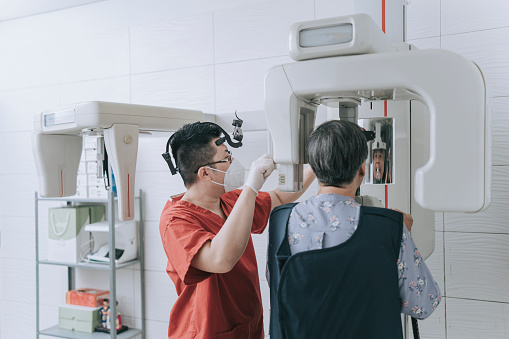Asian Chinese male dentist capturing medical x-ray image with senior woman patient in x-ray room.Dental digital tomography X-ray teeth Creating a panoramic picture of the teeth Professional dental diagnostics