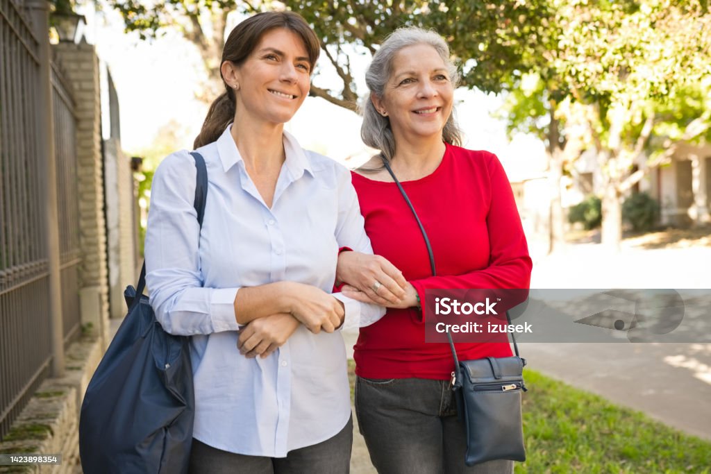 Senior woman and caregiver talking on footpath Smiling senior woman walking footpath with healthcare worker. Nurse and elderly female is with arm in arm. Nurse Stock Photo