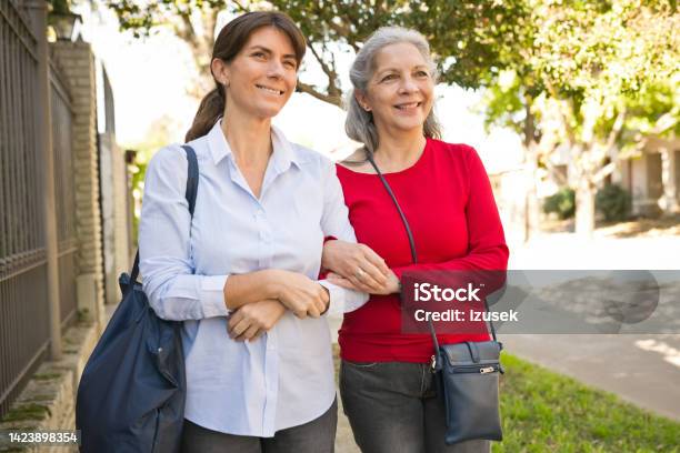 Senior Woman And Caregiver Talking On Footpath Stock Photo - Download Image Now - Nurse, Purse, 70-79 Years