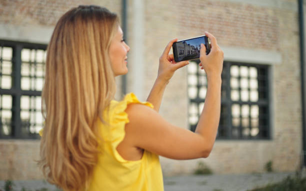 istock Beautiful woman taking pictures with her smartphone while exploring a city 1423899537