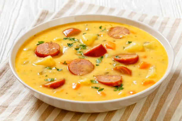 Kartoffelsuppe, German creamy potato soup with sausages in white bowl on white wooden table