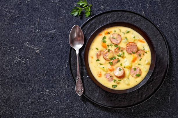 Kartoffelsuppe, German potato soup with sausages in black bowl on dark concrete table, horizontal view from above, flat lay, free space