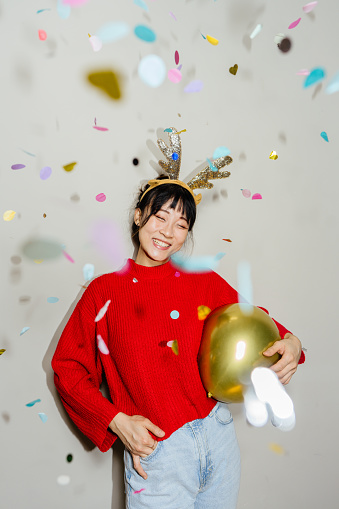 Portrait of a young , smiling woman looking at camera, posing for a photo during New Year's Eve, while colourful confetti falling over