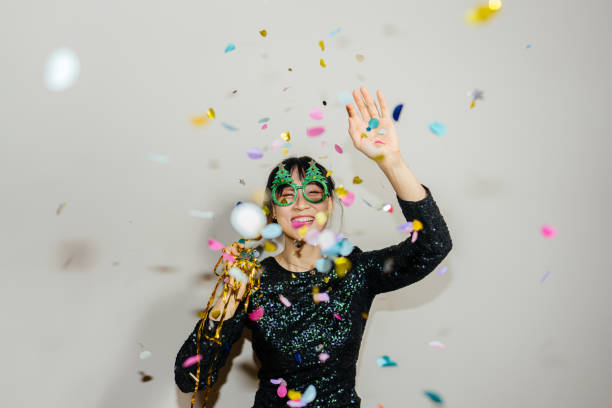 Photo of a young , smiling woman celebrating New Year's Eve, while colourful confetti falling over her during countdown