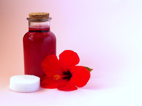 Homemade hibiscus skin care tonic. Glass bottle with toner and red flower.