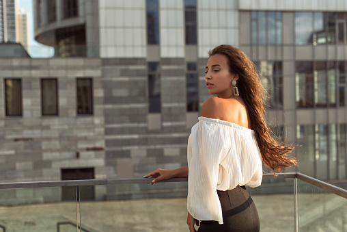 Charming girl in romantic outfit and wonderful hairstyle standing back in sunglasses and looking away from observation platform closeup. Trend look, relaxation on roof, sky, paris cityscape.