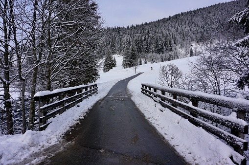 A snow-covered pedestrian bridge over a small river. Winter bridge in the forest. Wooden snow-covered pedestrian bridge in Bavaria. Winter Bridge in the Bavarian