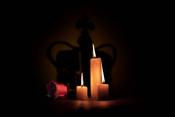 Lighted candles next to a rose on a black background with a cast shadow of a crown in memory of Queen stock photo