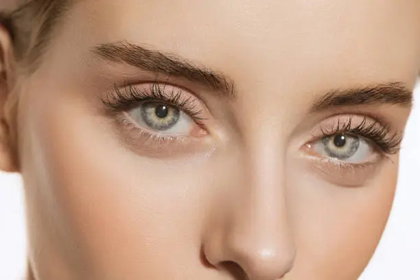 Photo of Blue eyes and perfect shapes of eyebrows. Close up portrait of beautiful young girl looking at camera. Concept of cosmetics, makeup, eco treatment, skin care.
