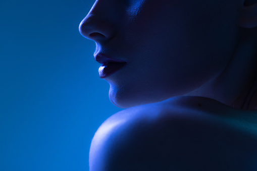 Night life. Cropped image of young woman in neon light on dark blue background. Monochrome. Cyberpunk style, beauty, cosmetics concept. Serious and thoughtful