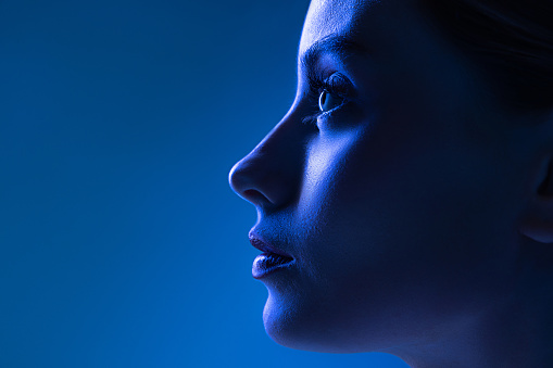 Closeup profile view of young pretty girl with well-kept skin isolated over dark blue background in neon light. Concept of high fashion, emotions, style, inspiration. Art portrait