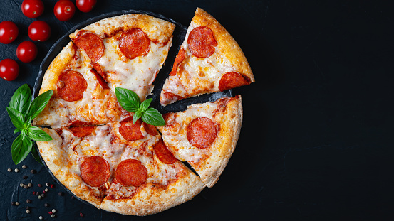Hot pepperoni pizza and cooking ingredients tomatoes basil on black concrete background. Top view of hot pepperoni pizza. With copy space for text.