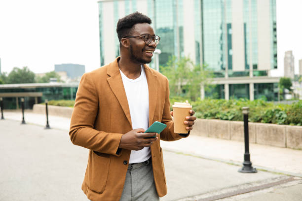 istock Young African businessman   on a coffee break walking and using smartphone 1423925993