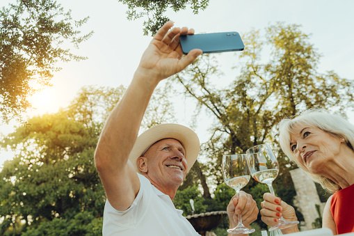 happy senior couple taking selfie while sitting at picnic table in garden. Happy senior couple making self portrait with mobile phone in courtyard.