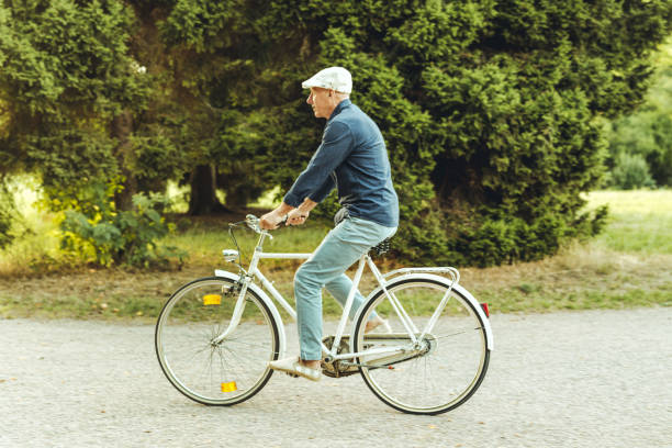 Happy active senior man riding bicycle in the park. Smiling senior man having fun riding vintage bike outdoors on sunny day.