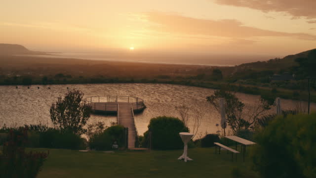 Wedding, venue and sunset with a lake, pier and green scenery for an outdoor celebration event. Stairs, view and sunset for a marriage ceremony against a romantic sky and picturesque backdrop