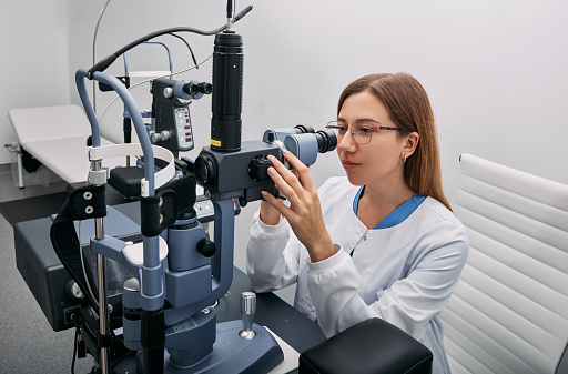 Portrait of caucasian female optometrist near ophthalmic equipment in modern ophthalmology office. Ophthalmology