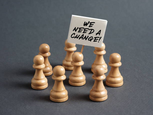 istock Chess pawn protester holding a sign banner with the message WE NEED A CHANGE surrounded by the crowd. Call for a political change. 1423932358