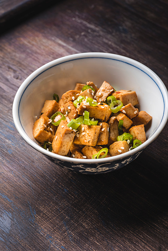 Fried tofu with sesame seeds, green onion and spices on the wooden vintage background. Homemade healthy vegetarian Asia and Japanese dish - fried tofu
