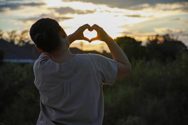 istock Heart shape with female hands over sunset sky background 1423934042