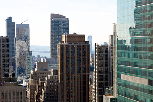 A view among Manhattan's chaotic jumble of Skyscrapers and lower buildings, with Ellis Island in the distance.