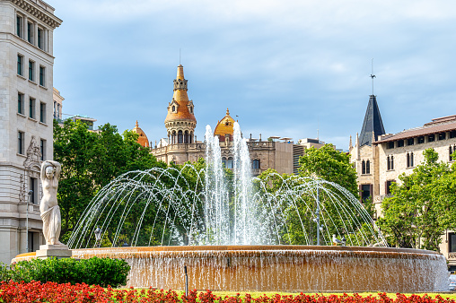 Barcelona, Spain - August 25, 2022: Close-up of a lovely water fountain in the Plaza de Catalunya. There are some large, tall buildings in the background.