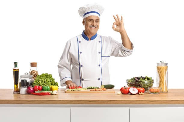 istock Mature male chef posing behind a counter with vegetables and gesturing good 1423936479