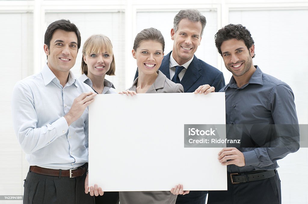 Businesspeople holding a blank poster and smiling Happy smiling business team holding a blank placard ready for your text or product. 20-29 Years Stock Photo