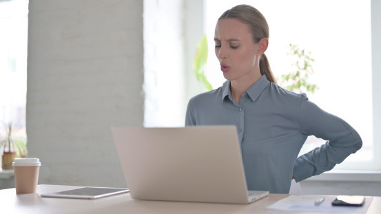 Young Woman having Back Pain while using Laptop in Office