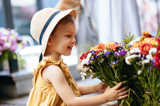 Portrait of a cute little girl in a yellow shirt and a hat looking at flowers and picking them up. She is smiling while looking at them.