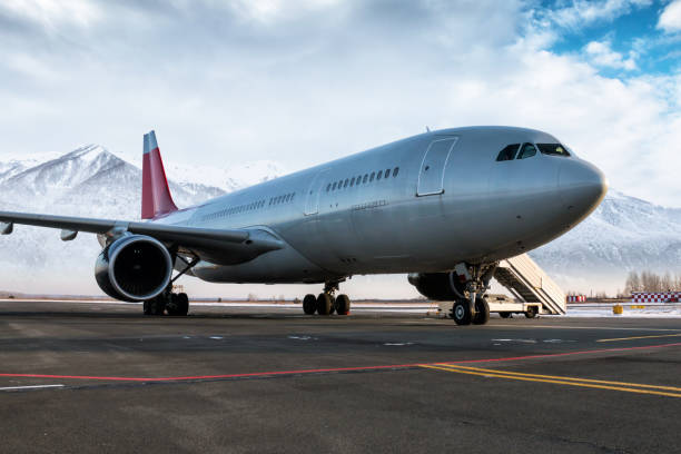 jetliner passeggeri a fusoliera larga e scale di imbarco sul grembiule dell'aeroporto sullo sfondo di alte montagne innevate panoramiche - airfield mountain snow airport foto e immagini stock