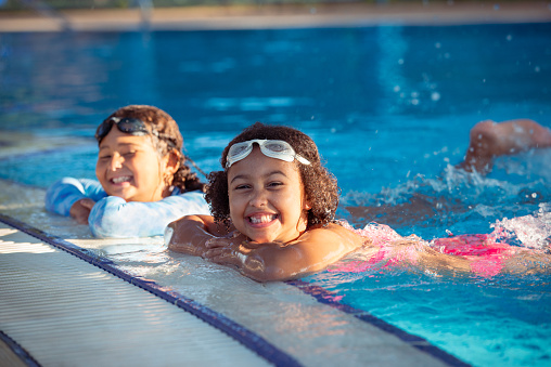 Portrait of multiracial elementary-age happy girls with swim goggles having fun on summer vacation, swimming in a pool.