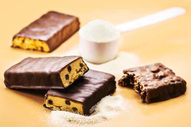 protein bar with sugar-free chocolate and spoonful of casey, whey or creatine in the background. Athletes' food supplementation stock photo