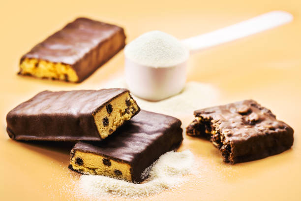 protein bar with sugar-free chocolate and spoonful of casey, whey or creatine in the background. athletes' food supplementation - protein concentrate imagens e fotografias de stock