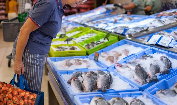 Senior caucasian woman shopping for fresh seafood at the supermarket retail store