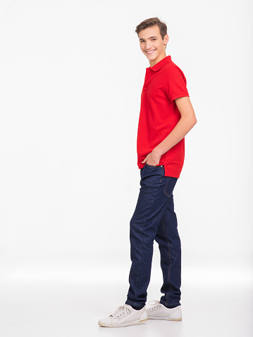 Photo of full length portrait of  young happy smiling man isolated on a white background. Portrait of smiling handsome guy posing at studio. Attractive teenage boy in a red shirt and dark blue jeans