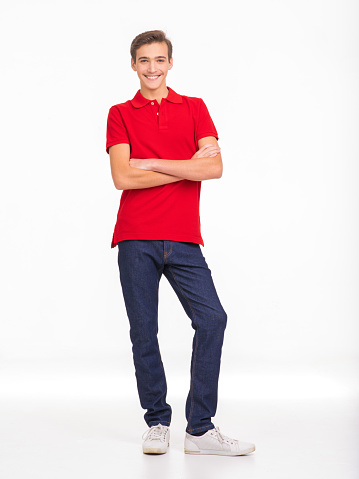 Photo of full length portrait of  young happy smiling man isolated on a white background. Portrait of smiling handsome guy posing at studio. Attractive teenage boy in a red shirt and dark blue jeans