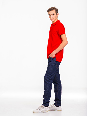 Photo of  young  confident man looking at camera. Full length Portrait of handsome guy with a calm emotions, posing at studio. Attractive male face. Teenager in a red shirt and blue jeans.