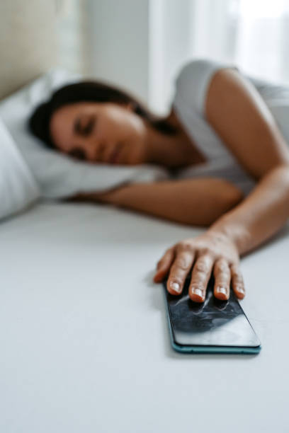 une jeune femme qui fait dormir son alarme sur un téléphone intelligent - clock time clock hand urgency photos et images de collection