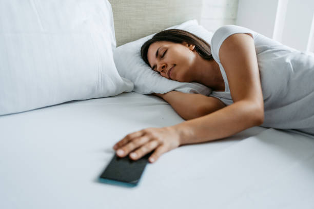 une jeune femme qui fait dormir son alarme sur un téléphone intelligent - clock time clock hand urgency photos et images de collection